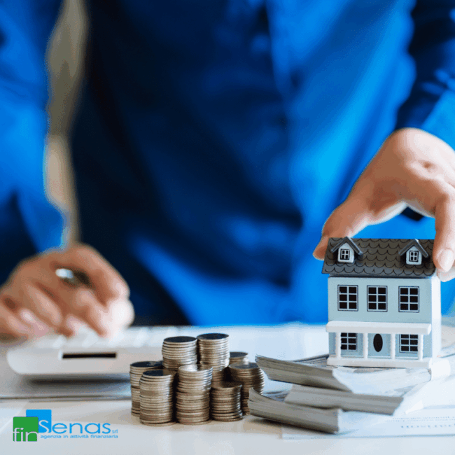 Casetta in miniatura appoggiata su documenti accanto a pile di monete e una calcolatrice, simbolo di tasse sulla casa e IMU