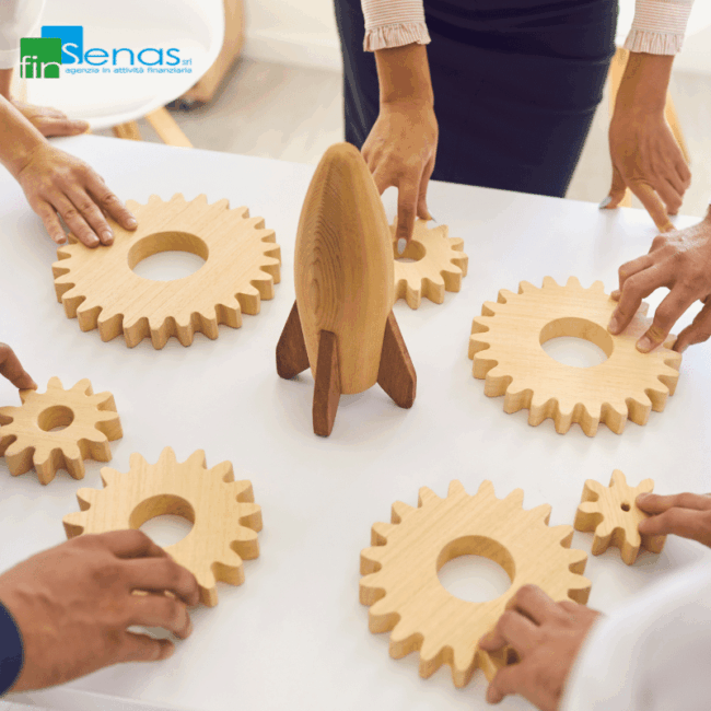 Mani di più persone sistemano ingranaggi di legno attorno a una figura a forma di razzo su un tavolo.