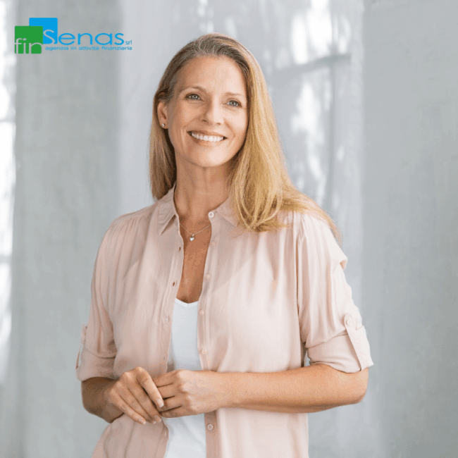 Donna sorridente con camicia chiara, in piedi in un ambiente luminoso con sfondo neutro