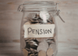 Barattolo di vetro pieno di monete con etichetta “pensione”, simbolo del risparmio e dell’incremento dell’assegno pensionistico.