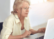 Donna anziana usa un laptop per informarsi su come cumulare reddito e pensione, simbolo della gestione dei diritti pensionistici.