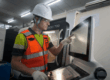 Tecnico industriale davanti a un macchinario CNC mentre utilizza un pannello di controllo digitale in un ambiente produttivo.