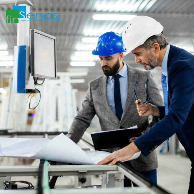 Come proporre il noleggio operativo ai tuoi clienti se sei un fornitore Due uomini in cantiere industriale che indossano caschi di protezione e controllano progetti su tavolo con documenti e monitor, immagine rappresentativa del noleggio operativo per fornitori.
