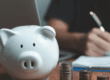 Salvadanaio bianco con monete accanto a documenti e penna, rappresentando la gestione economica e gli aspetti previdenziali della pensione di reversibilità.