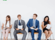 Quattro candidati seduti in attesa di un colloquio di lavoro mentre consultano curriculum e documenti, rappresentativi delle difficoltà delle aziende nel trovare personale adeguato.