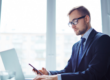 Professionista al computer utilizza lo smartphone durante un’attività lavorativa, rappresentando i contatti tra finanziaria e datore di lavoro nella Cessione del Quinto.